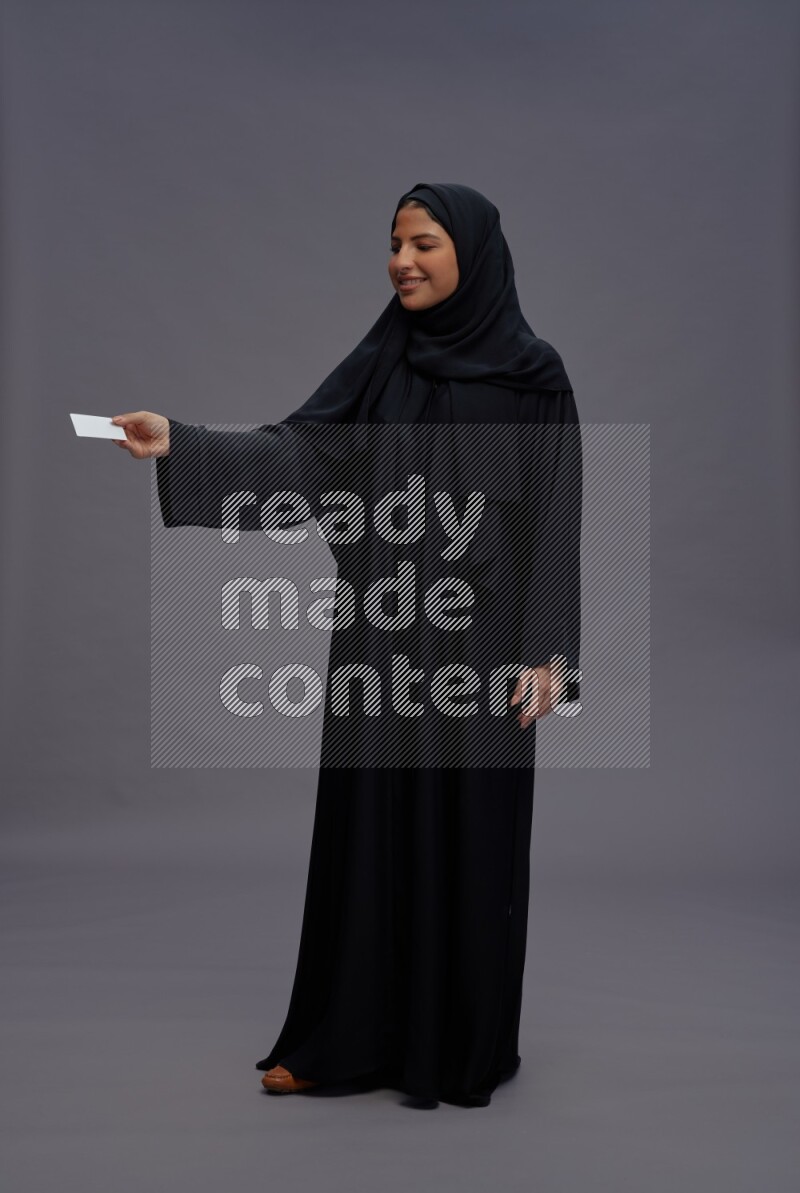Saudi woman wearing Abaya standing holding ATM card on gray background
