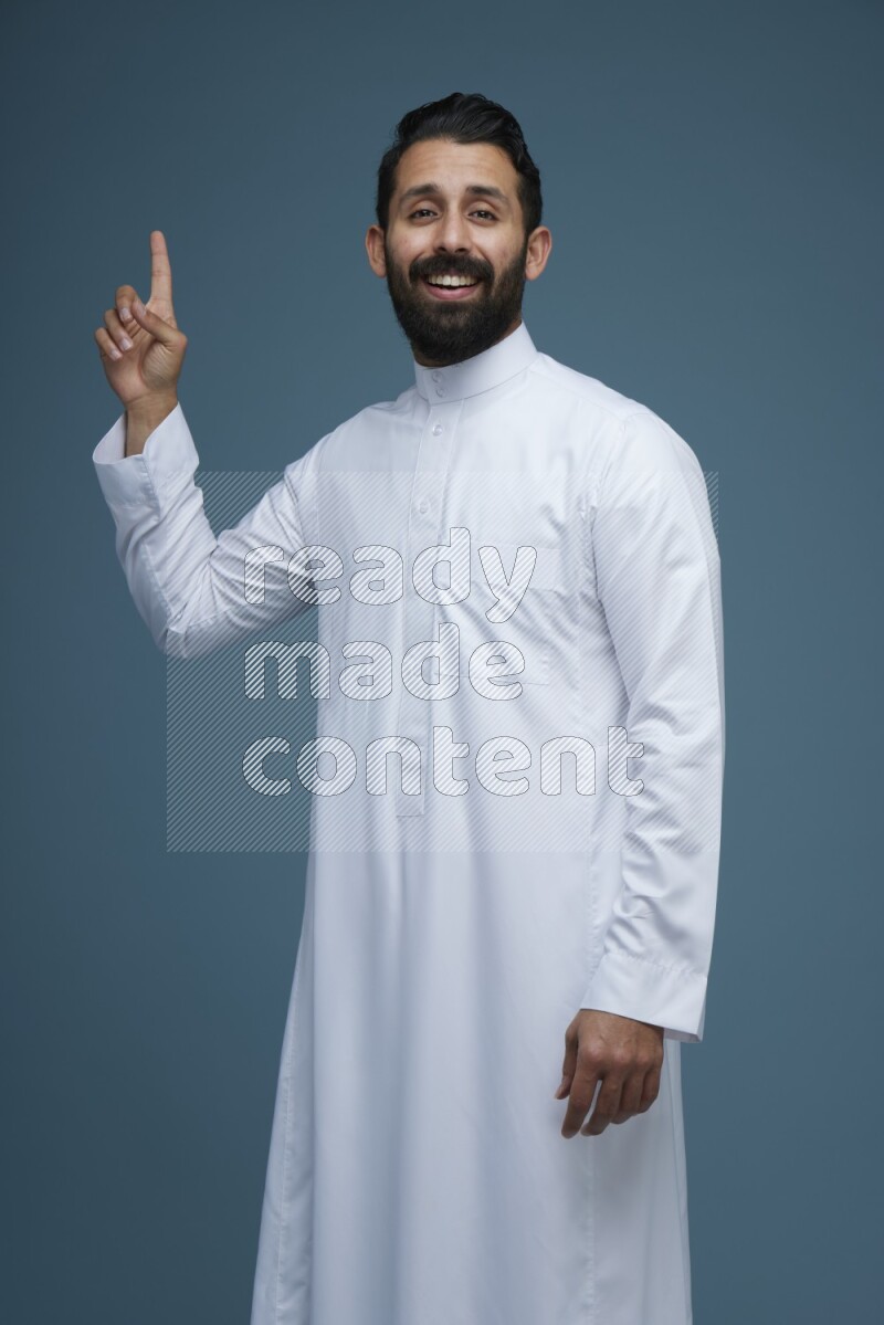 A man pointing in a blue background wearing Saudi Thob