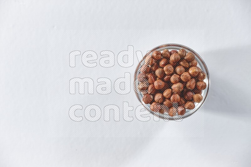 وعاء زجاجي ممتلئ بحبوب البندق المقشرة على خلفية بيضاء