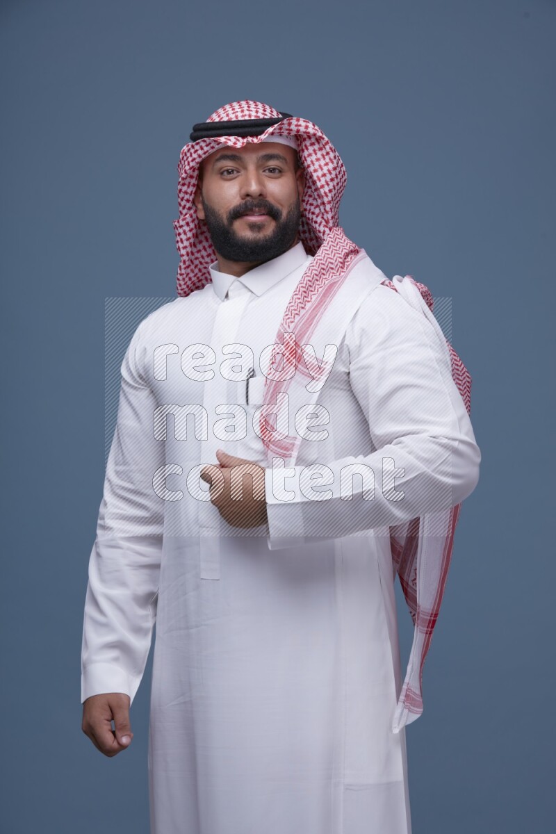 A Saudi man posing on blue background wearing Thob and Shomag