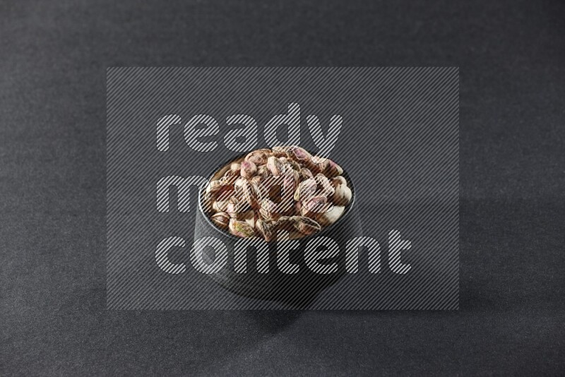 A black pottery bowl full of peeled pistachios on a black background in different angles