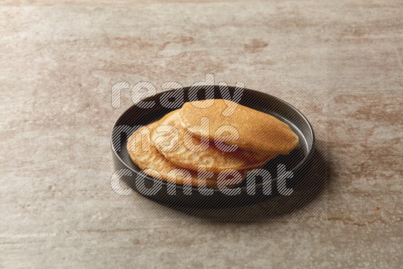 Three stacked plain pancakes in a black plate on beige background
