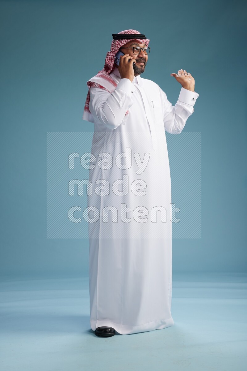 Saudi Man with shimag Standing talking on phone on blue background