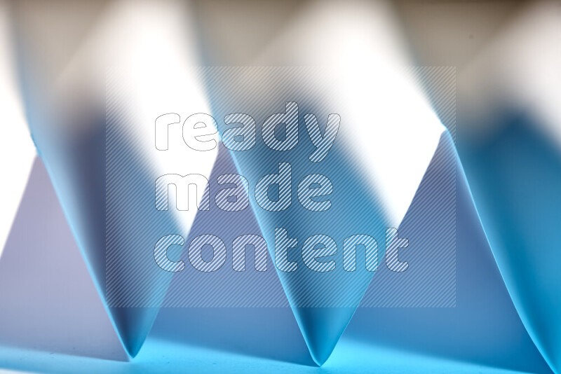 A close-up abstract image showing sharp geometric paper folds in white and blue gradients