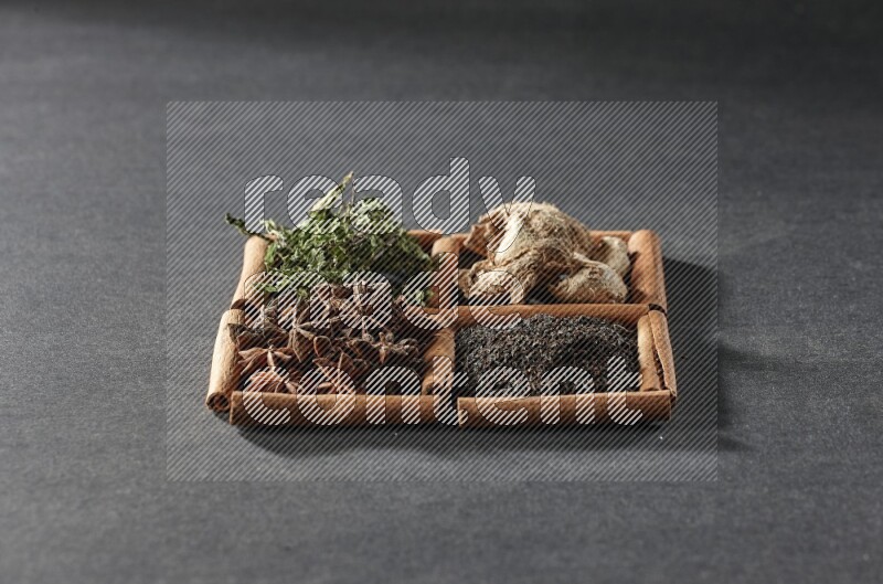 4 squares of cinnamon sticks full of black tea, dried ginger, dried mint leaves and star anise on black flooring