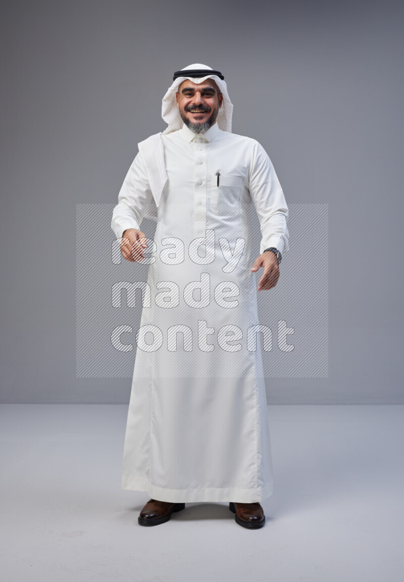 Saudi man Wearing Thob and white Shomag standing interacting with the camera on Gray background