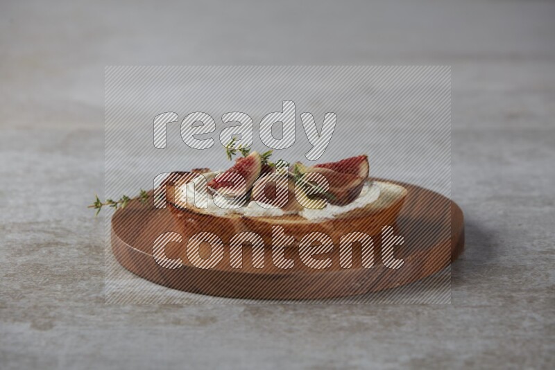 quarters of figs with cream cheese on toasted sourdough slice on a wooden board on textured grey background