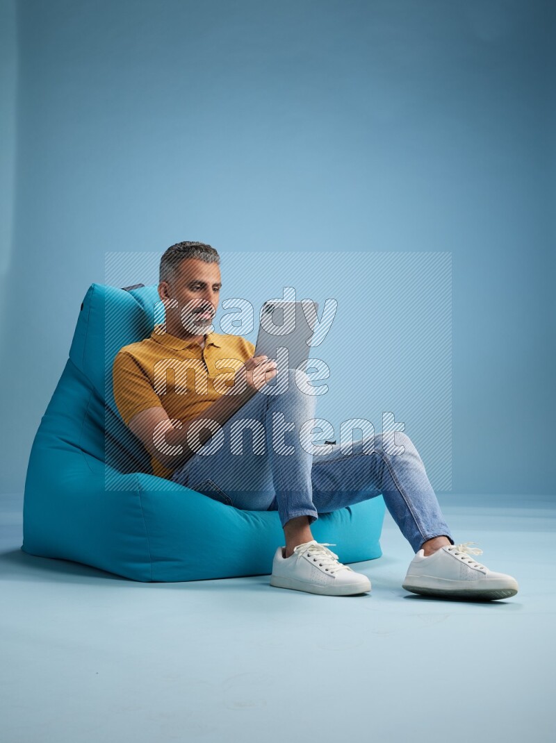 A man sitting on a blue beanbag and working on tablet