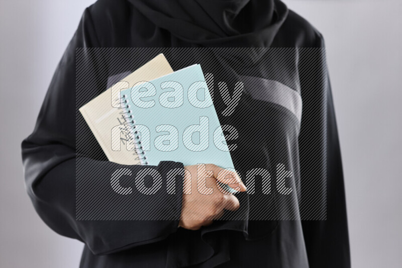 A woman in abaya holding books and a board in different positions (back to school)