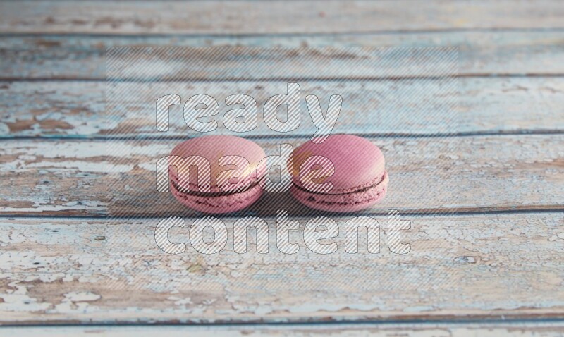 45º Shot of two Purple Strawberry macarons on light blue wooden background