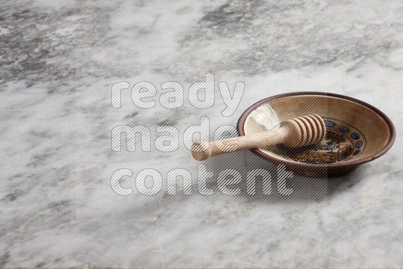 Decorative pottery plate with wooden honey dipper in it on grey marble background