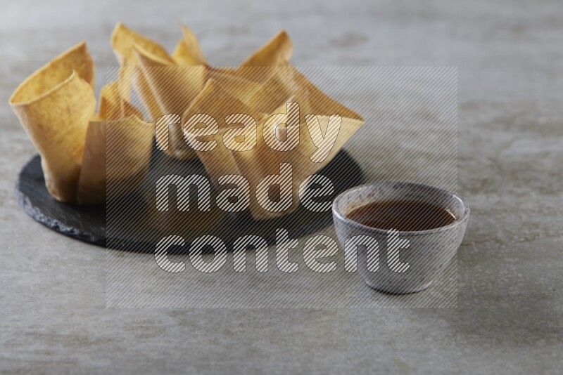 wonton cups with soy sauce ramkin on circle slate on grey textured counter top