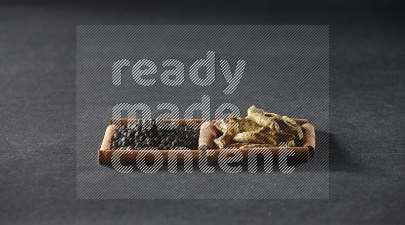 مربعان من أعواد القرفة ممتلئان بحبوب الفلفل الأسود وأصابع الكركم علي خلفية سوداء