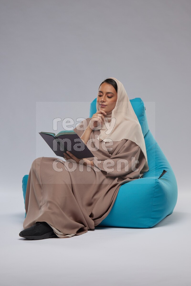 A woman sitting on a blue beanbag and reading a book