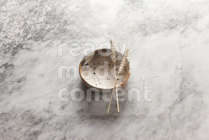 Wheat stalks on multicolored pottery bowl on grey marble background