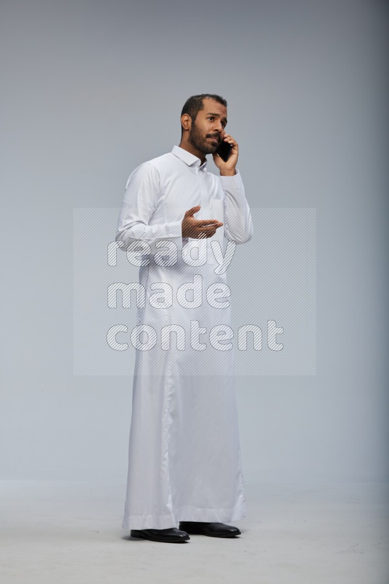Saudi man wearing Thob standing talking on phone on Gray background