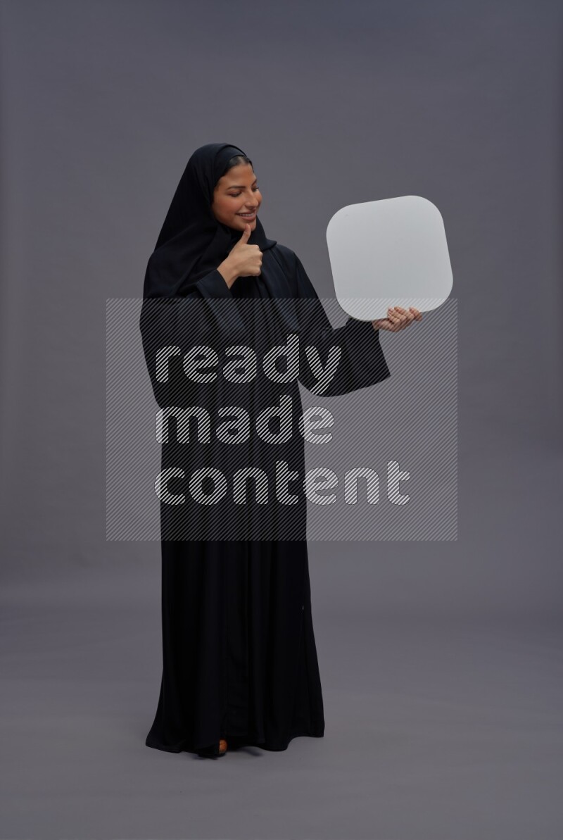 Saudi woman wearing Abaya standing holding social media sign on gray background