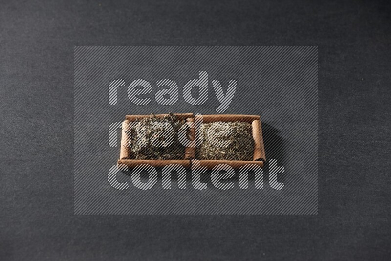 مربعان من أعواد القرفة ممتلئان بحبوب الكمون والريحان المجفف علي خلفية سوداء