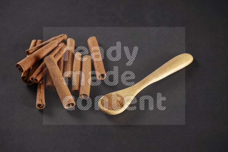 Cinnamon sticks stacked beside a wooden spoon full of cinnamon powder on black background