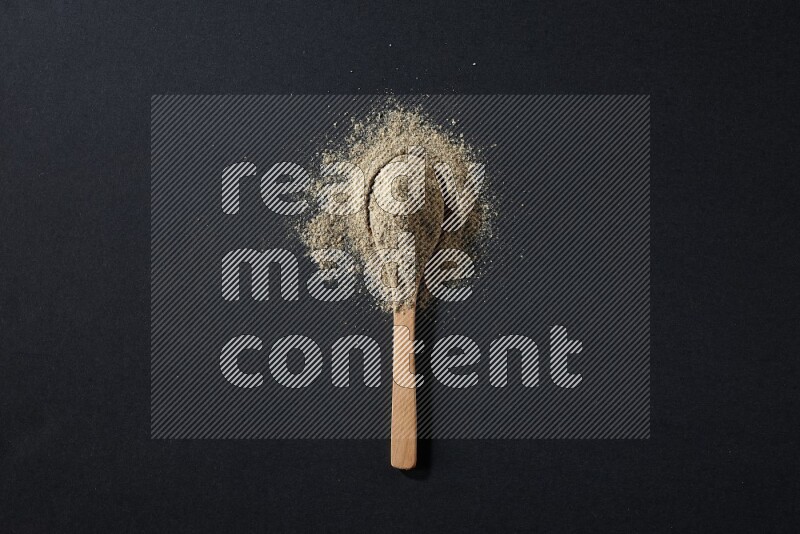 A wooden spoon full of cardamom powder and powder spreaded on black flooring