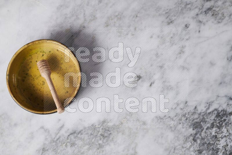 Multicolored pottery oven plate with wooden honey dipper in it on grey marble background