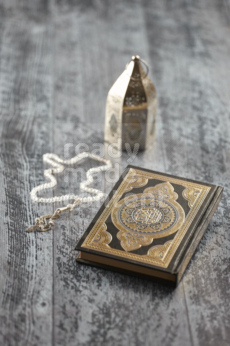 A silver lantern with different drinks, dates, nuts, prayer beads and quran on grey wooden background