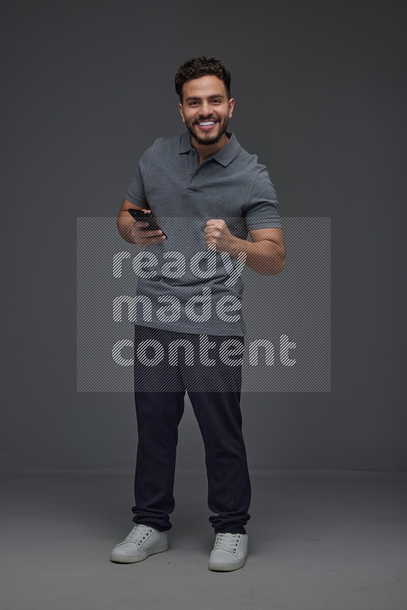 A man wearing casual standing and using his phone eye level on a gray background