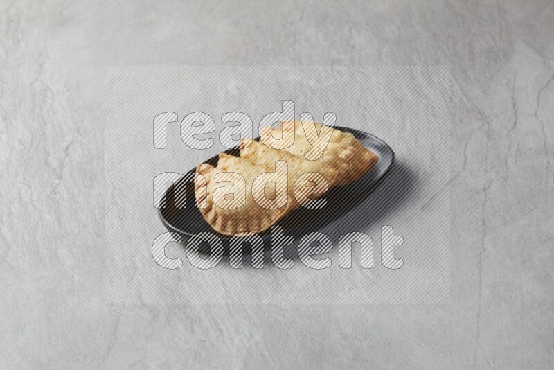 Five fried sambosas in an oval shaped black plate on a gray background