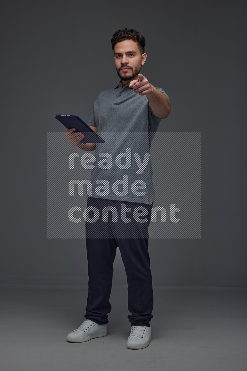 A man wearing casual standing and using his tablet and making multi hand gestures different angles eye level on a gray background