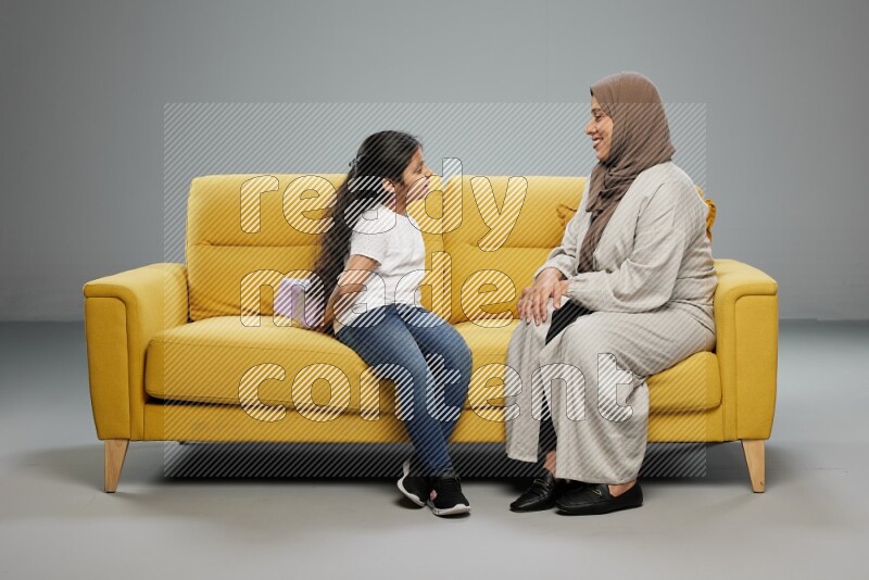 A girl sitting hiding a gift behind her back for her mother on gray background