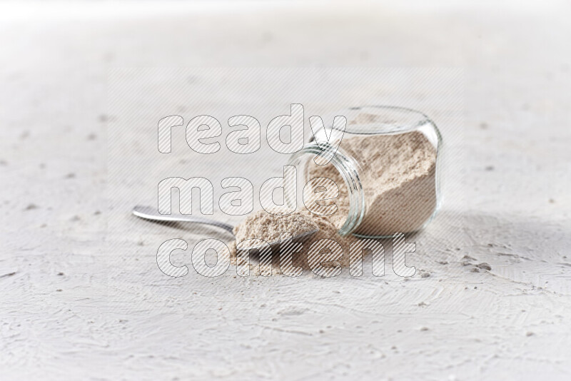 A glass jar full of onion powder flipped with some spilling powder on white background