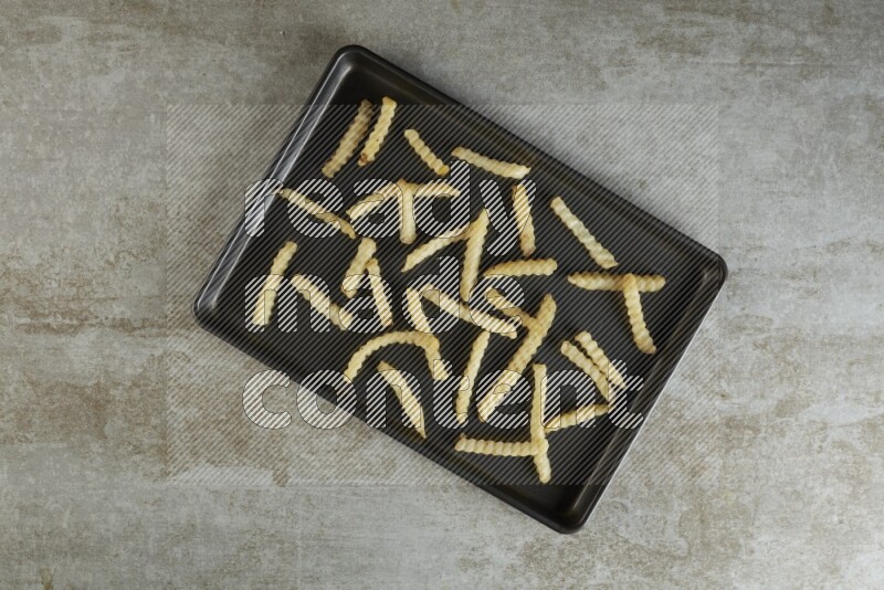 crinkle fries in a black stainless steel rectangle tray on grey textured counter top