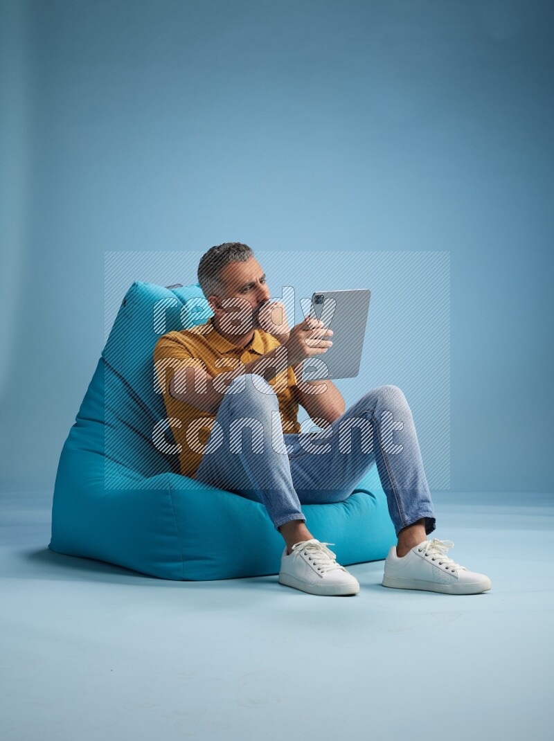 A man sitting on a blue beanbag and working on tablet