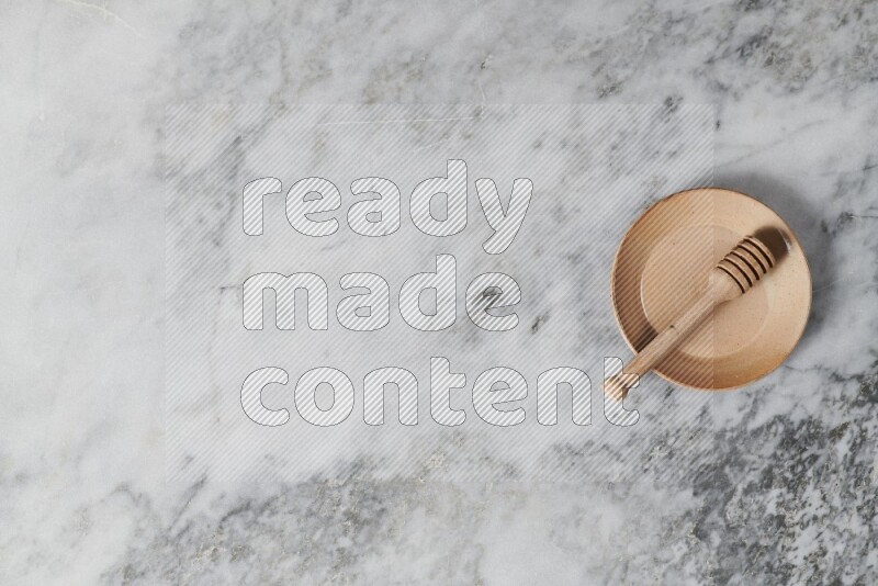 Beige pottery plate with wooden honey dipper in it on grey marble background