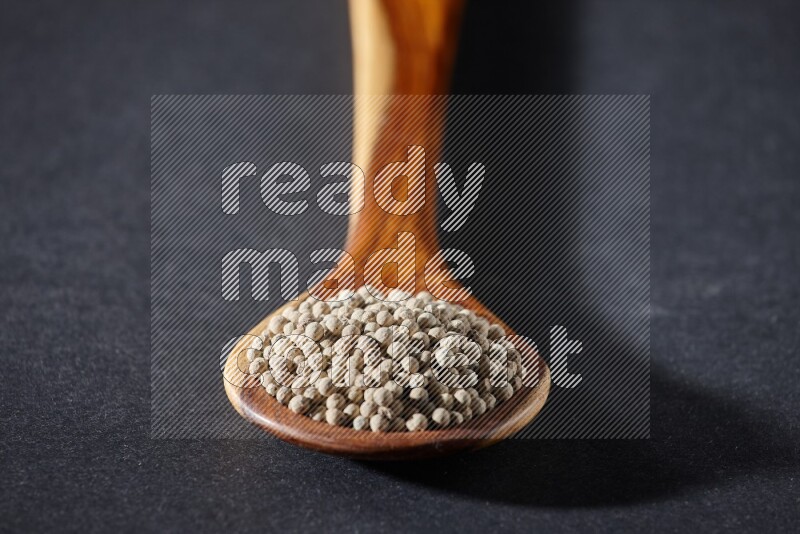 A wooden ladle full of white pepper beads on black flooring