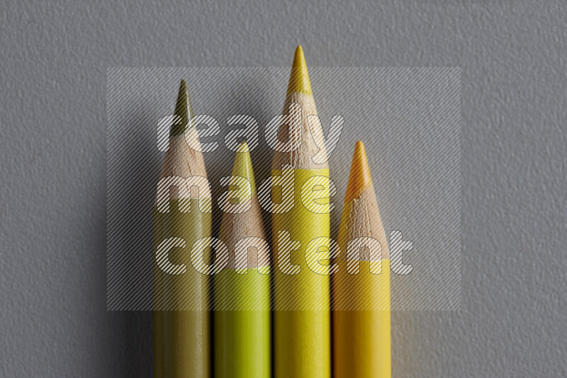 A collection of sharpened colored pencils arranged showcasing a gradient of yellow hues on grey background