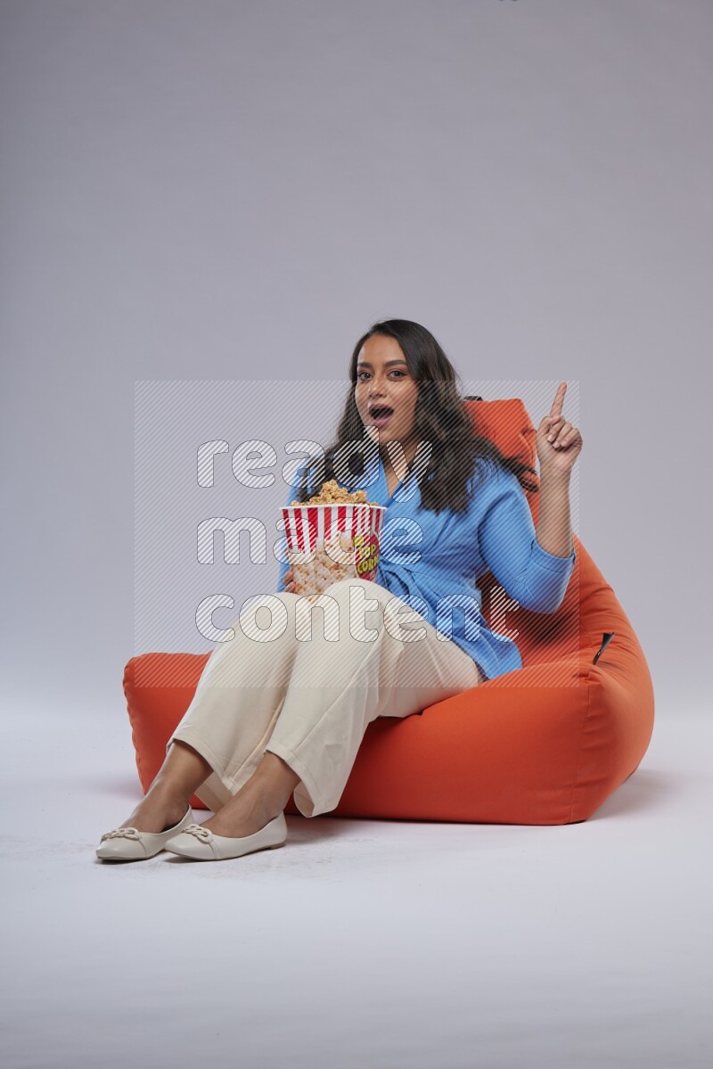 A woman sitting on an orange beanbag and eating popcorn