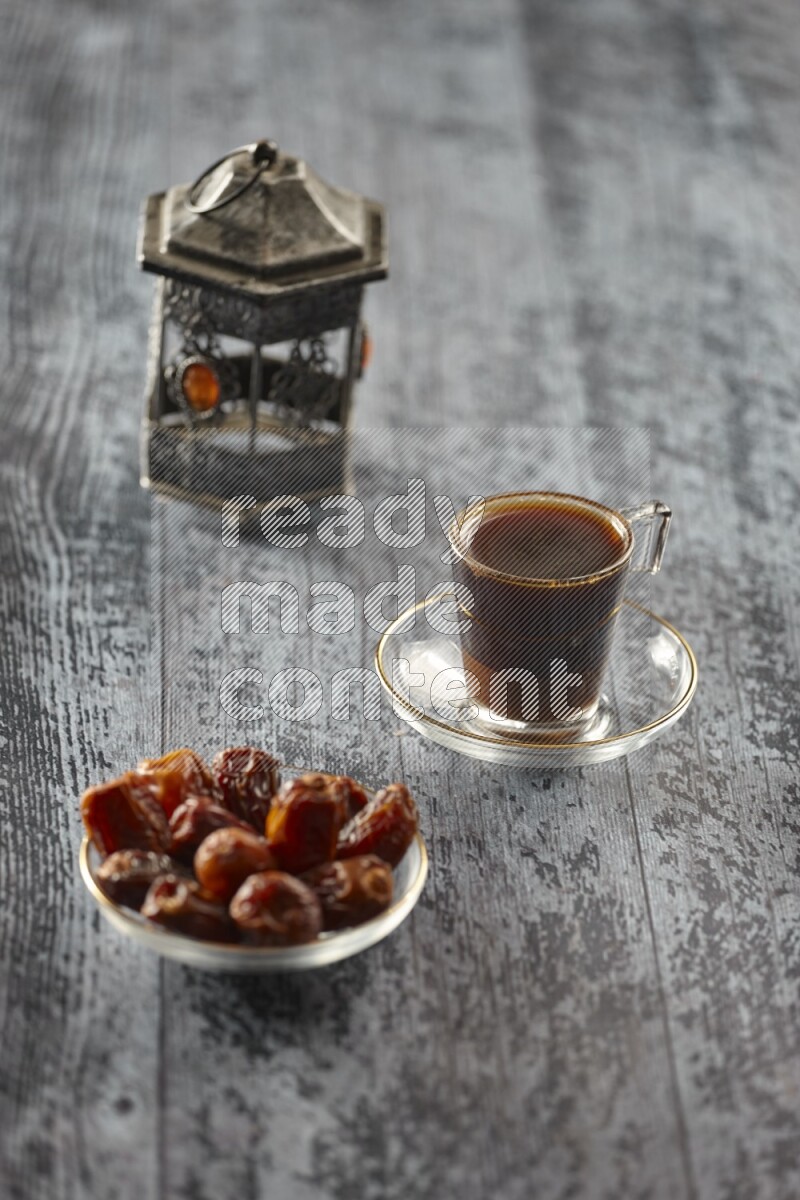A silver lantern with different drinks, dates, nuts, prayer beads and quran on grey wooden background