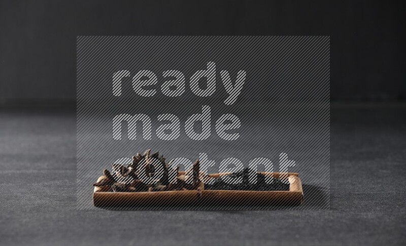 مربعان من أعواد القرفة ممتلئان بحبة البركة السوداء واليانسون النجمي علي خلفية سوداء