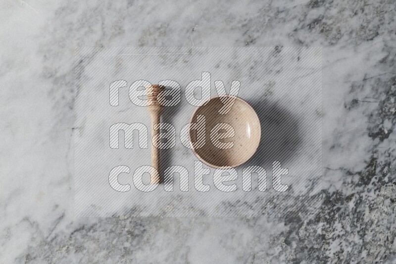 Beige pottery bowl with wooden honey dipper on the side on grey marble background