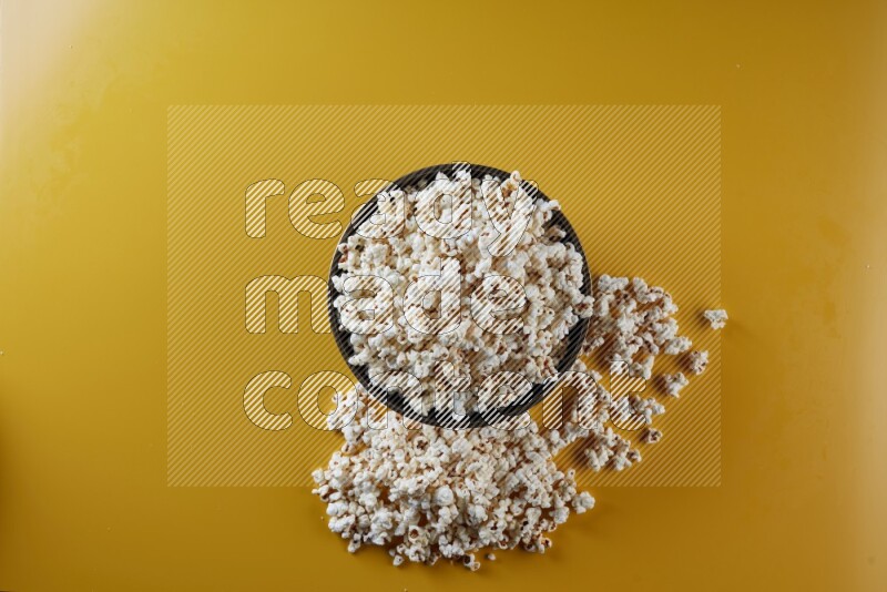 A copper ceramic bowl full of popcorn with popcorn beside it on a yellow background in different angles