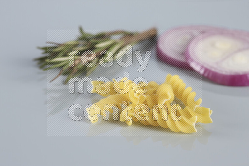 Raw pasta with different ingredients such as cherry tomatoes, garlic, onions, red chilis, black pepper, white pepper, bay laurel leaves, rosemary, cardamom and mushrooms on light blue background