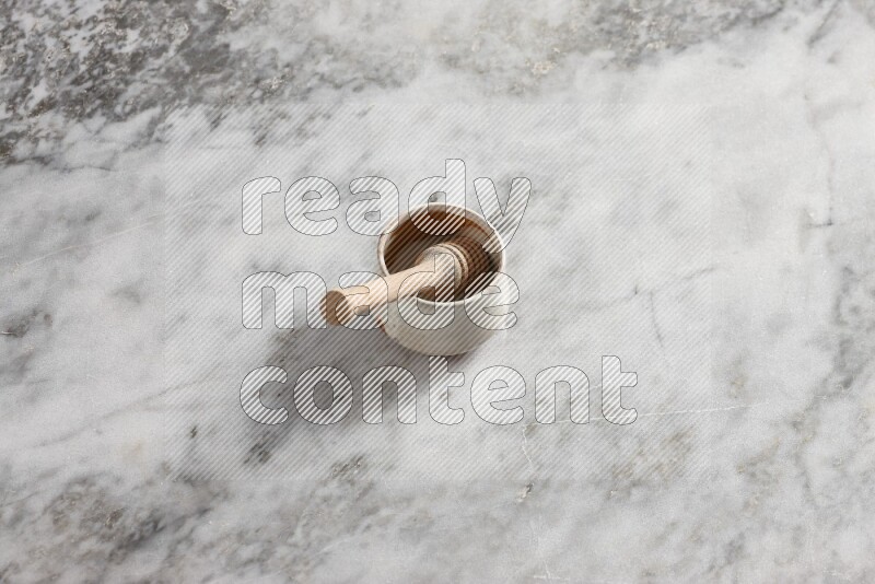 Beige pottery bowl with wooden honey dipper in it on grey marble background
