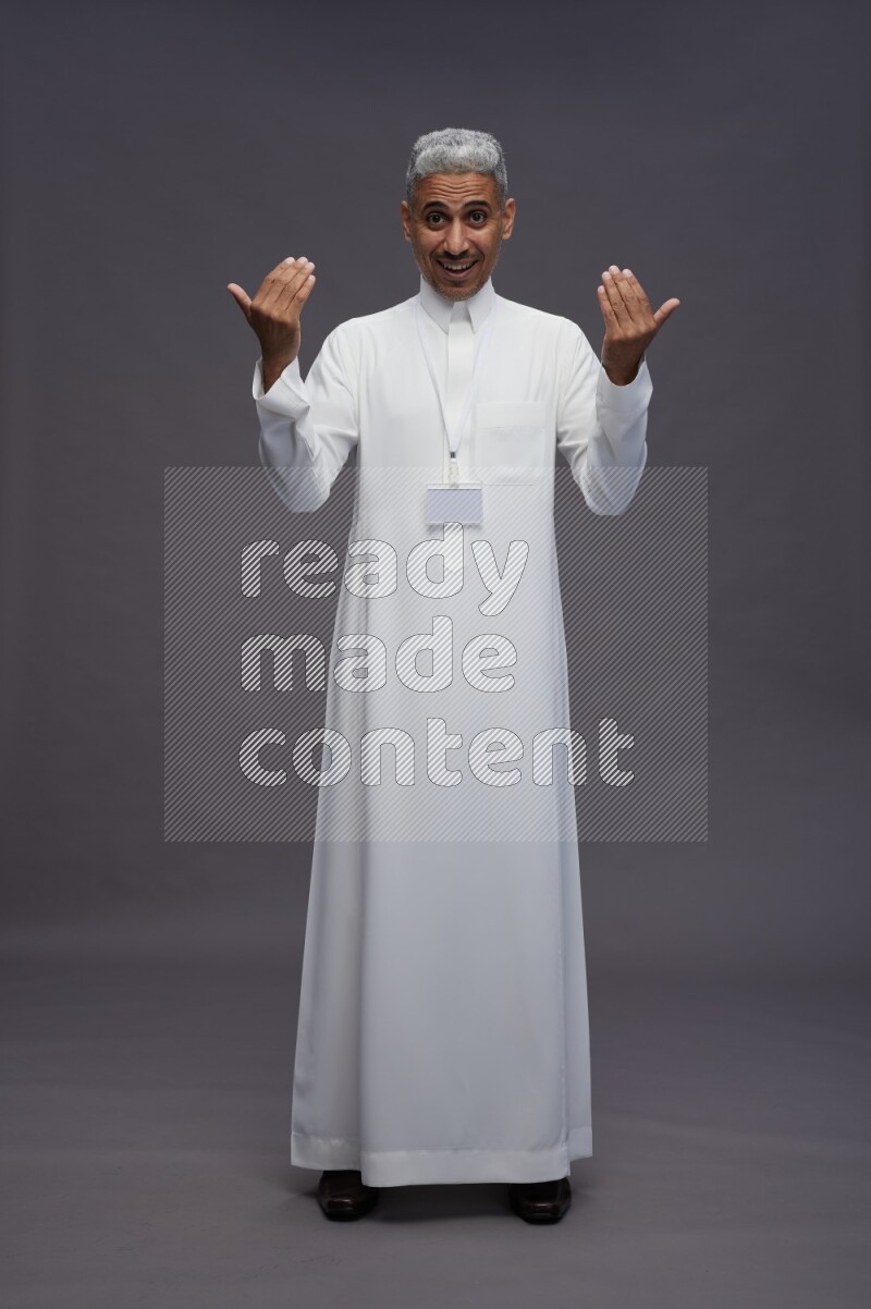 Saudi man wearing thob with neck strap employee badge standing interacting with the camera on gray background