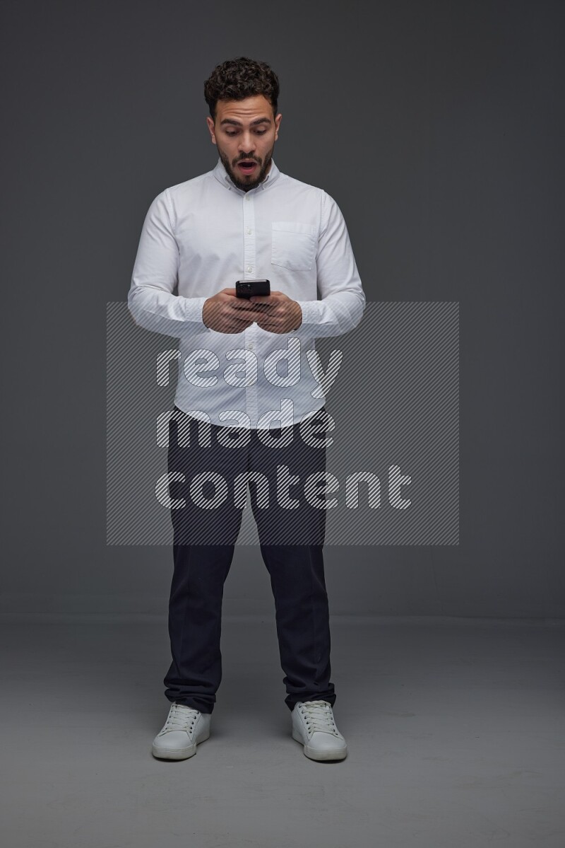 A man wearing smart casual standing and using his phone eye level on a gray background