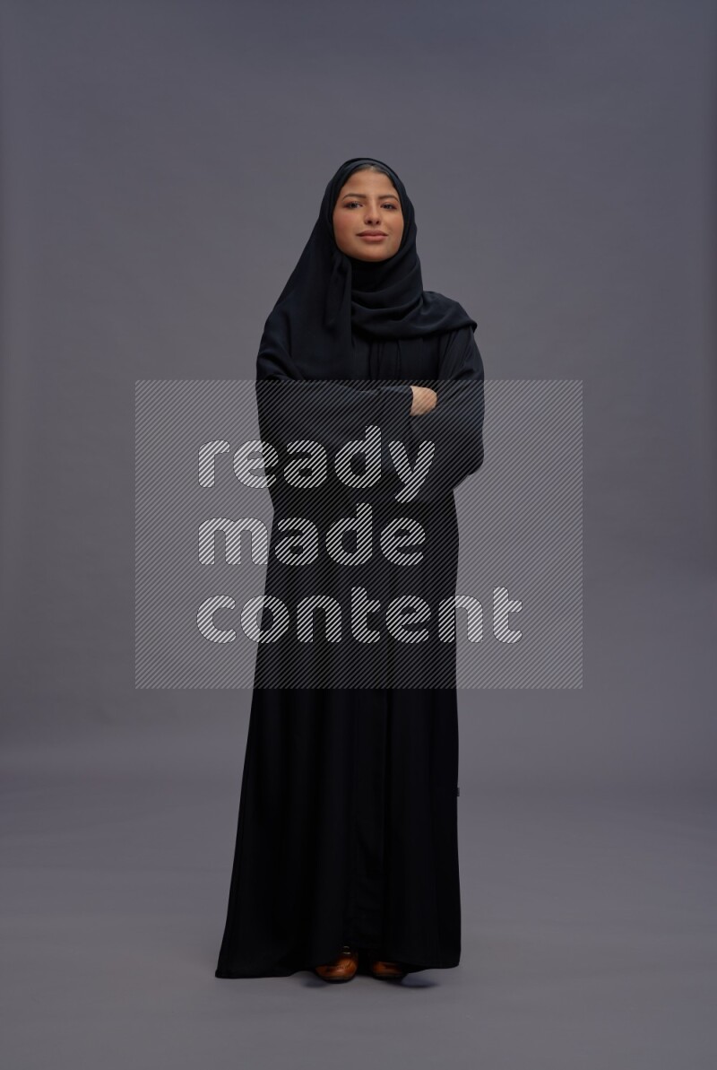 Saudi woman wearing Abaya standing with crossed arms on gray background