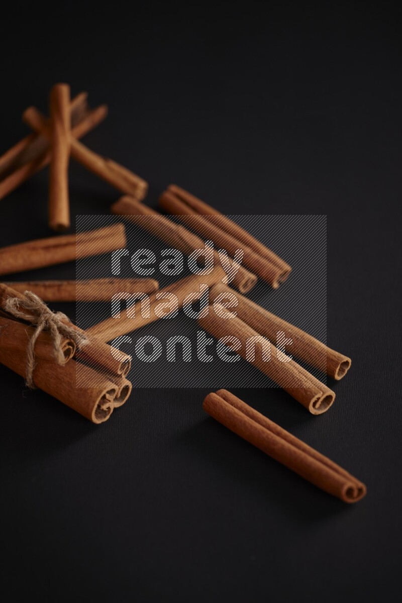4 Cinnamon sticks stacked and bounded with more sticks in the background on black flooring