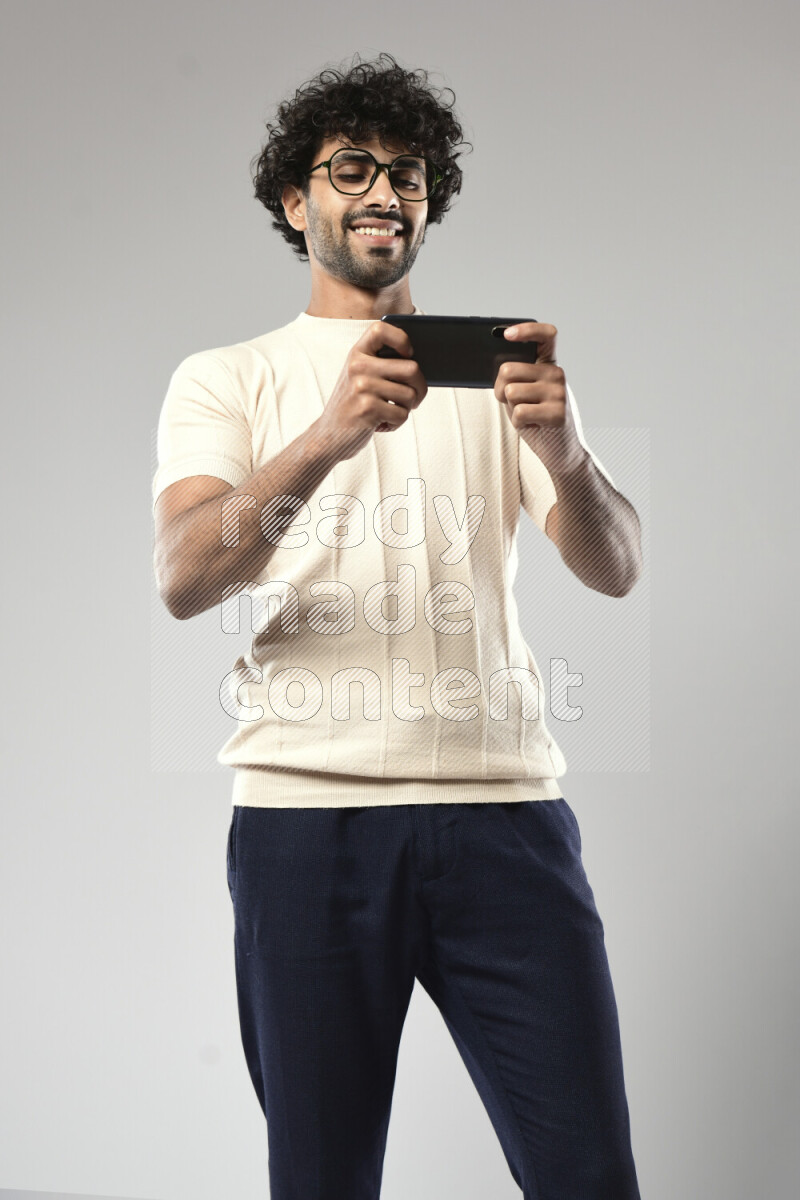 A man wearing casual standing and gaming on the phone on white background