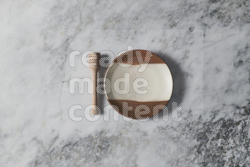 Multicolored pottery plate with wooden honey dipper on the side on grey marble background