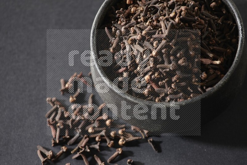 وعاء فخاري أسود ممتلئ بحبوب القرنفل علي خلفية سوداء